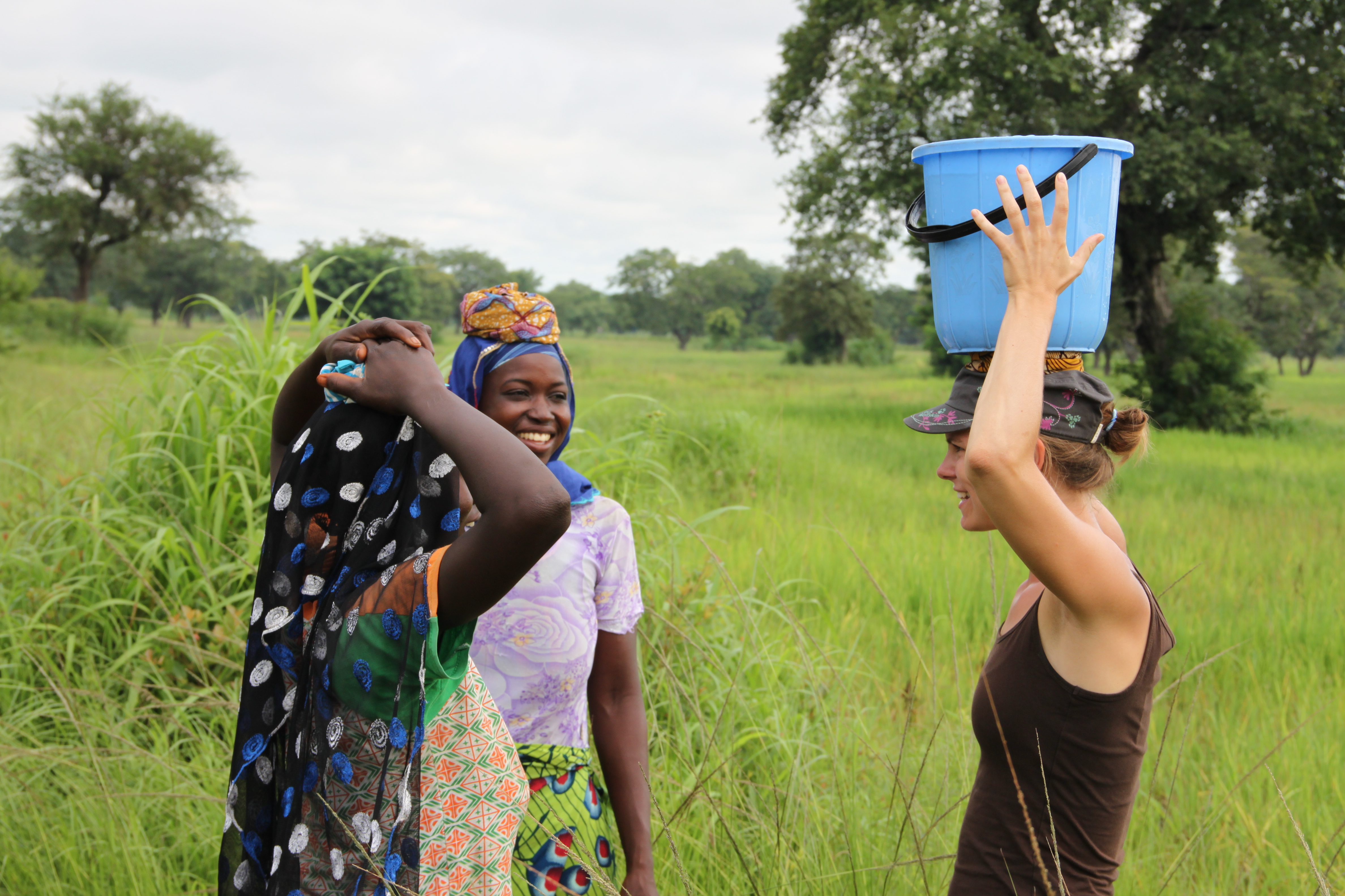 Frauen aus Ghana und Österreicherin unterhalten sich. Allte tragen Eimer auf dem Kopf. 