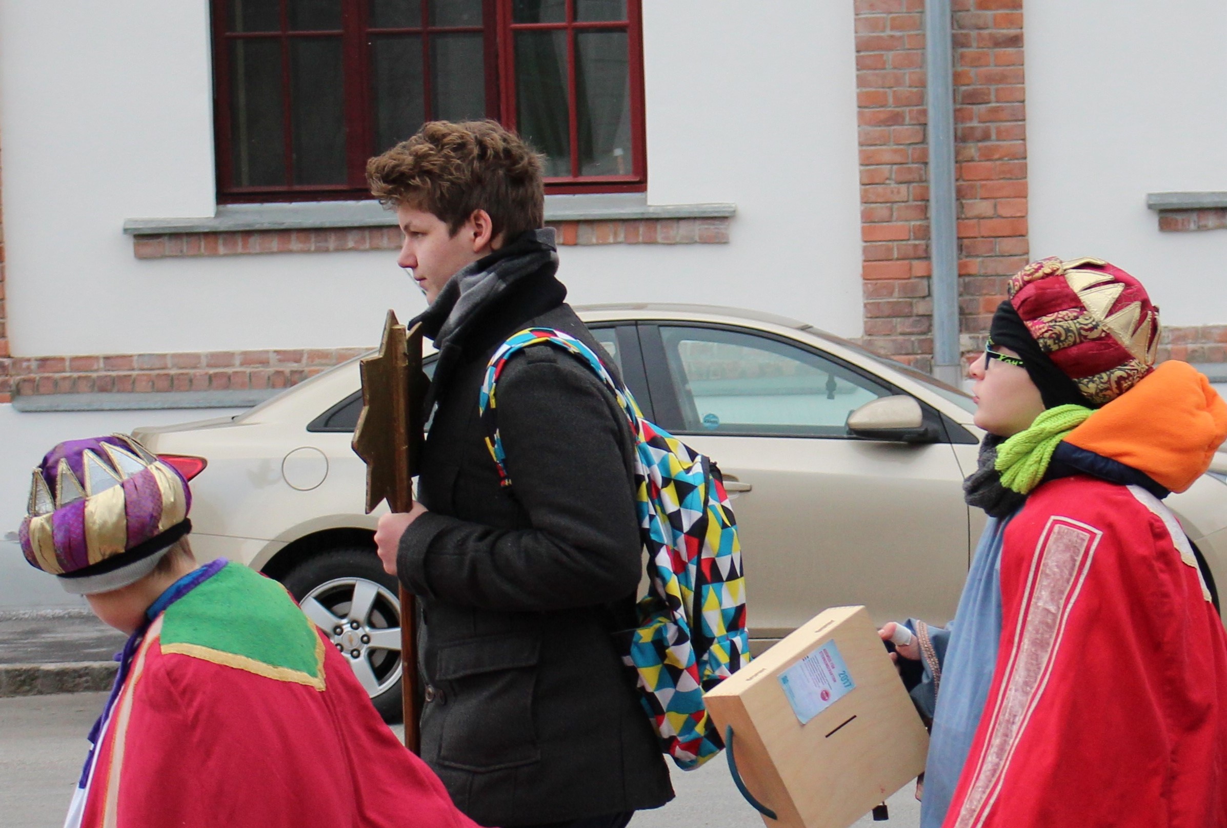 Sternsingergruppe geht Straße hinunter, zwei Sternsinger mit Begleitperson. 